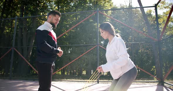 Sporty Woman with Personal Trainer Doing Exercises with Resistance Band Outside