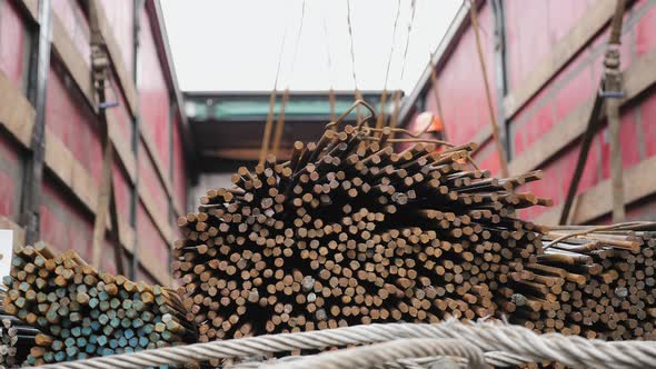 Workers Using a Crane Unload a Bundle of Steel Rods