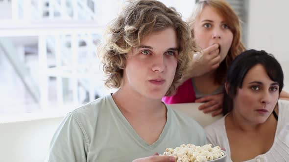 Three teenagers watching TV and eating popcorn