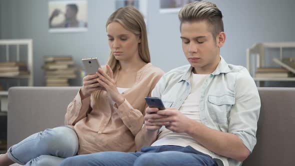 Couple in Love Indifferently Sitting on Couch Looking at Their Smartphones