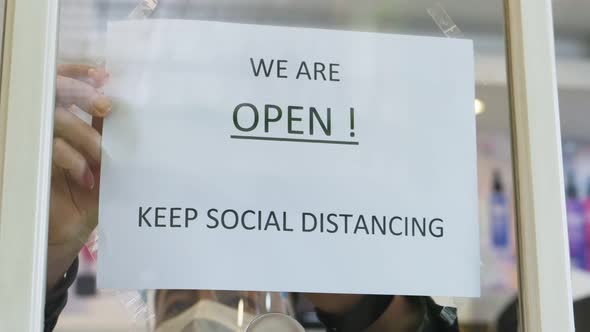 Hairdresser wear face mask turning sign from closed to open on a door shop after quarantine is over.