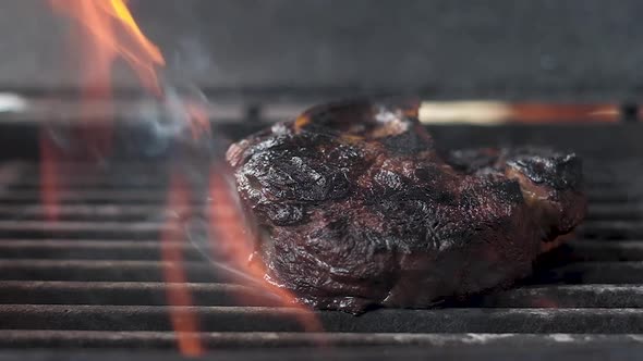 big piece of meat on bone fried on grill in flames. piled on top of  peppercorns