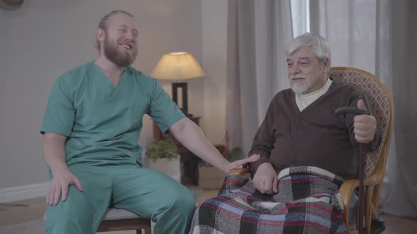 Positive Adult Caucasian Man in Nurse Uniform Chatting with Mature Male Retiree in Nursing Home