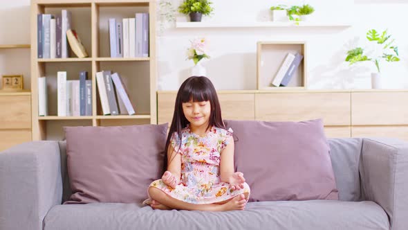 Calm of Asian child cute making yoga meditation with inhale and exhale. Sit on couch for focusing mi