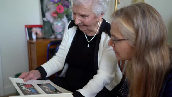 Closeup of elderly woman smiling as she holds photos on her lap looking at photos in the lap of a pr
