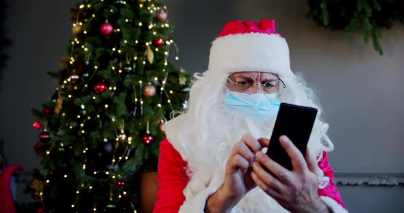 Santa Claus with Medical Mask in Living Room and Chatting By Smartphone with Video Chat. Close Up