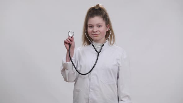 Portrait of Confident Girl Showing Stethoscope Looking at Camera Smiling Standing at White