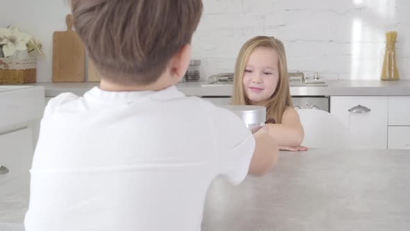 Unrecognizable Caucasian Boy in White T-shirt Giving Gift Box To Pretty Little Lady. Cute Girl