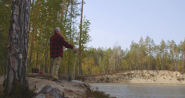 Angling at Weekend, Middle-aged Fisherman Is Standing on Coast of Forest River Under High Trees and