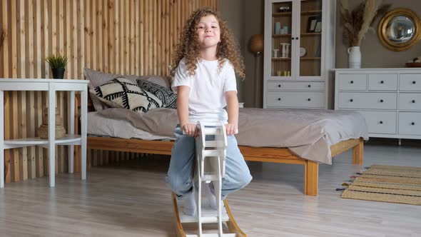 Amazed Small Preschooler Girl Rocks on Rocking Horse By Bed