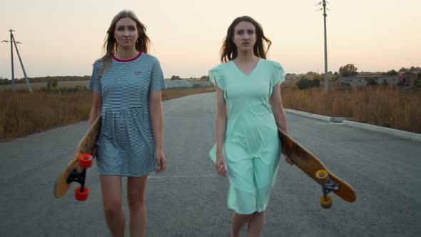 Young Women Wearing Colorful Sundresses Are Walking with Their Longboards, 