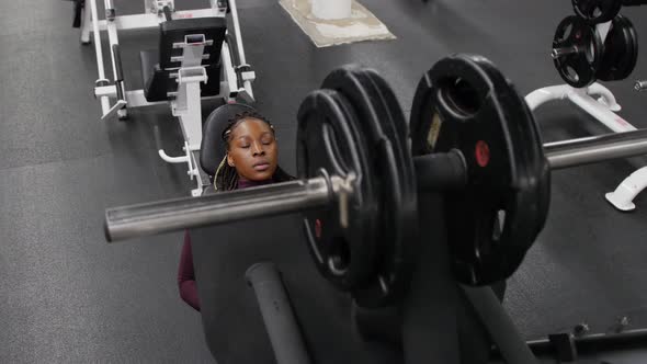 Sports Training Indoors Black Woman Sits Down on a Exercise Equipment and Starts Training Her Legs