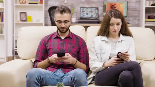 Caucasian Couple Sitting on the Couch Browsing on Their Phones