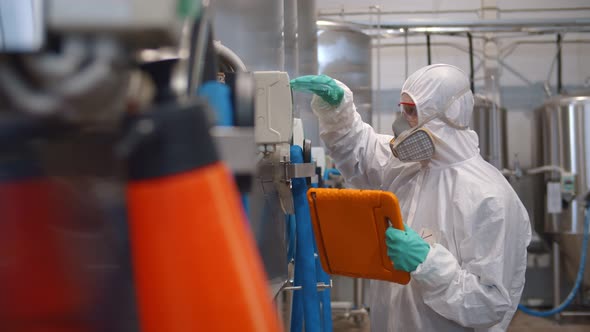 Professional Technologist in Safety Suit and Mask Using Tablet in Production Plant