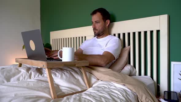 Man sitting in bed starting to work on laptop