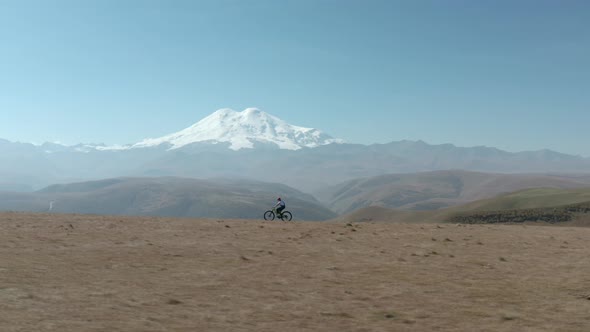 Bicycle Woman Riding Bike on Snowy Mountain Peak Background. Tourist Girl Traveling on Sport Enduro