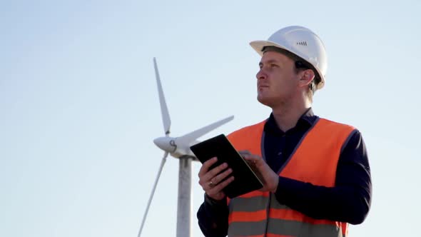 Engineer Caucasian Appearance Stands Beside a Windmill and on Studying the Data Looking at Tablet