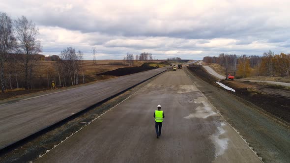 Worker in a Helmet, is on the Construction of the Road. Aerial Shoot