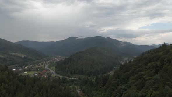 Flying towards valley in Ukraine with tiny village and road. Aerial.