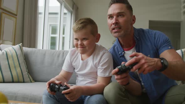 Happy caucasian father with son sitting in living room and playing video games