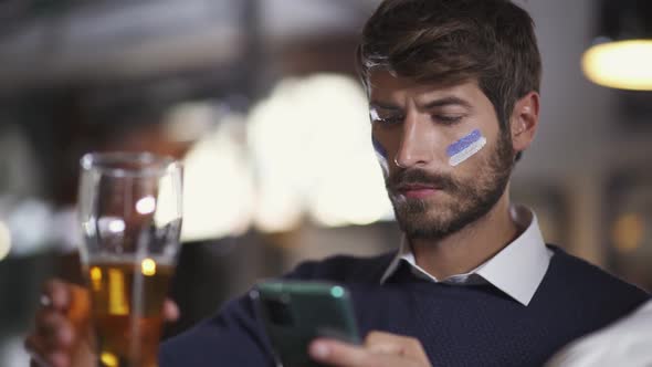 Football Fan Sits in a Bar During a Football Match Drinks Beer and Using Their Smartphone Surfing