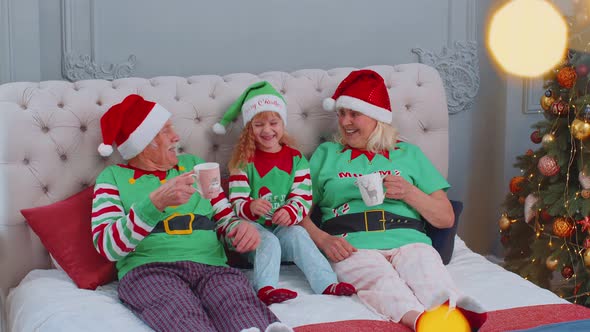 Senior Couple Grandparents Drinking Hot Tea on Bed with Granddaughter Toddler Kid Christmas Morning