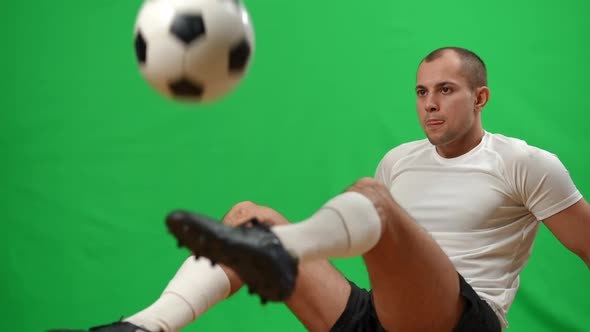 Professional Confident Footballer Juggling Catching Ball with Legs Sitting on Green Screen and