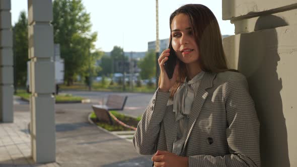 Young Woman in a Business Suit Talking on the Phone While Standing on the Street