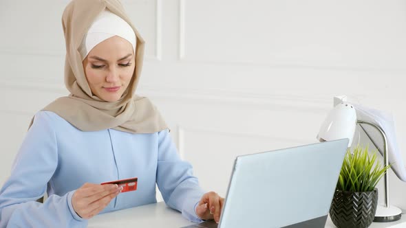 Muslim Woman in Hijab is Buying Online with a Credit Card and Laptop