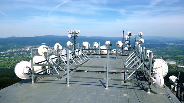 White Parabolic Antennas on the Rooftop of a Building, a Town, a Forest and the Blue Sky