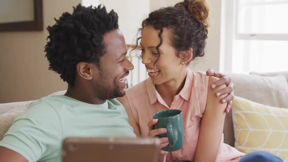 Happy biracial couple sitting on sofa and having video call on smartphone