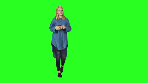 Blonde Teenager Girl Calmly Walking and Drinking Coffee on Green Screen Background. Chroma Key, Shot