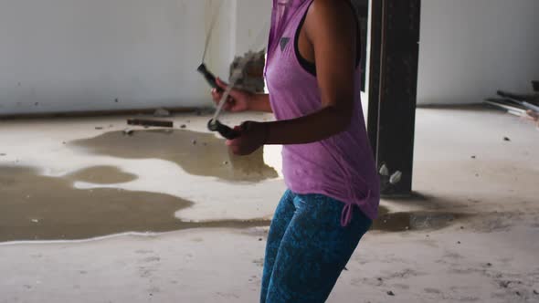 African american woman wearing hoodie skipping rope in an empty urban building