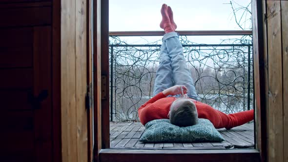 Man on the Balcony Lights a Cigarette with His Legs Thrown Up Killing Time