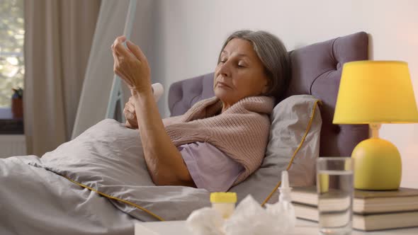 Sick Retired Woman Lying in Bed Measuring Temperature with Digital Thermometer