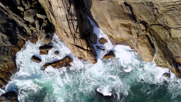 Aerial top down view of sea waves breaking on the rocky coastline. Locked off