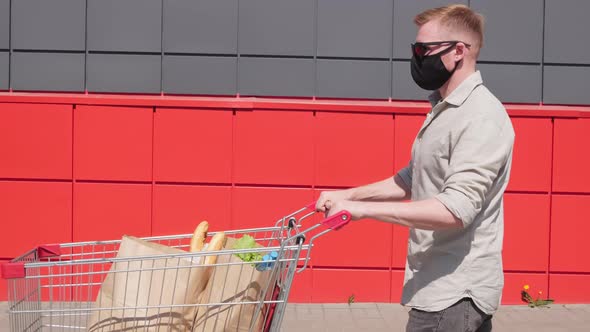 Man in Face Mask Pushing Cart with Groceries