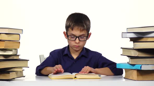 Boy Sits at the Table Leafing Through the Pages of a Book. White Background.