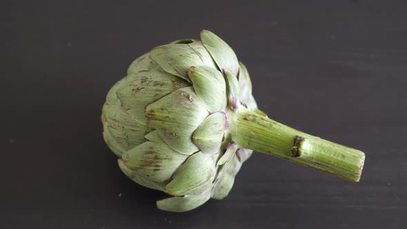 One Whole Fresh Artichoke Rotating on Black Table