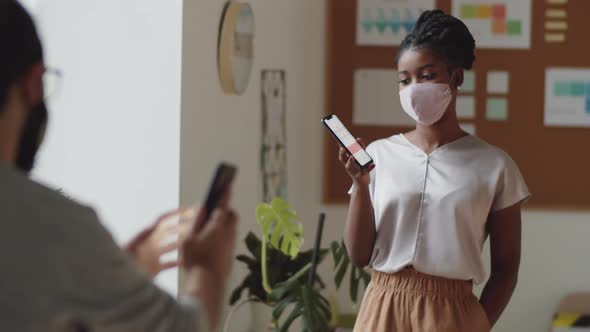 Office Workers in Masks Discussing Business Graphs on Smartphones