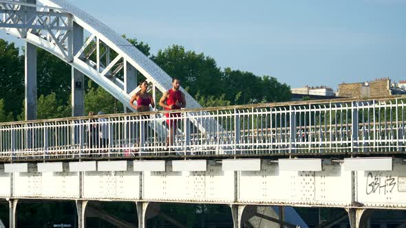 A man woman couple running across a bridge with the Eiffel Tower