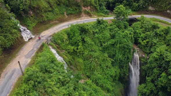 A Motorbike Traveler Driving on the Small Road with Waterfalls and Greenery.