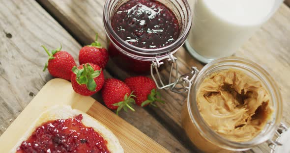 Peanut butter and jelly sandwich on wooden tray with milk and strawberries on wooden surface