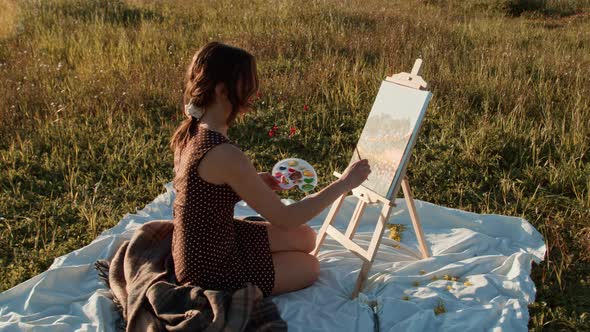 Young girl paints a picture sitting on the grass