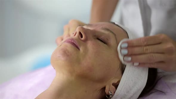 The girl beautician clears the face of the client, preparing for the procedures