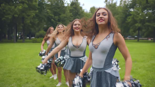 Portrait of Beautiful Cheerleader Girls Standing in Line and Dancing with Pompoms Outdoors