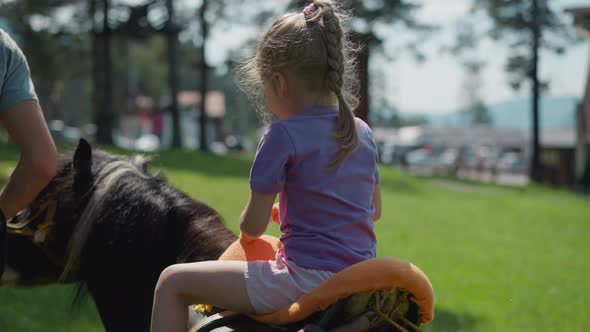 Little Child Rides Pony with Instructor Along City Garden