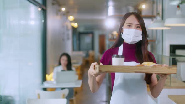 Attractive asian female cafe worker wears face mask and gloves giving takeaway food