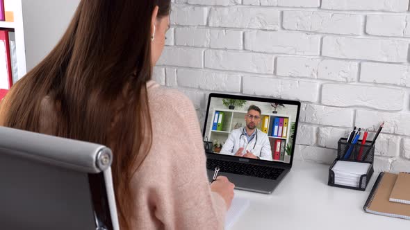 Woman student study at home office online video call laptop, writes in notebook