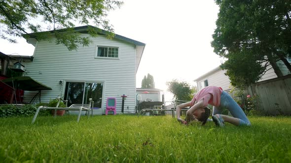 The Child Is Engaged in Acrobatics at Sunset in Back Yard. Play Game. Slow Motion